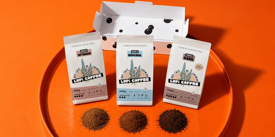 Boîte de découverte Lupi Coffee ouverte avec les sachets Original, Intense et Dark et trois petits tas de mouture de teintes différentes